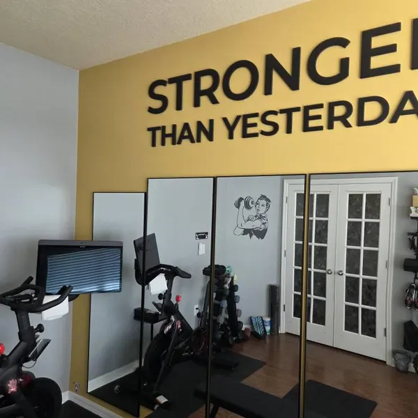 STRONGER THAN YESTERDAY lettering on a yellow wall above a customer's gym mirrors