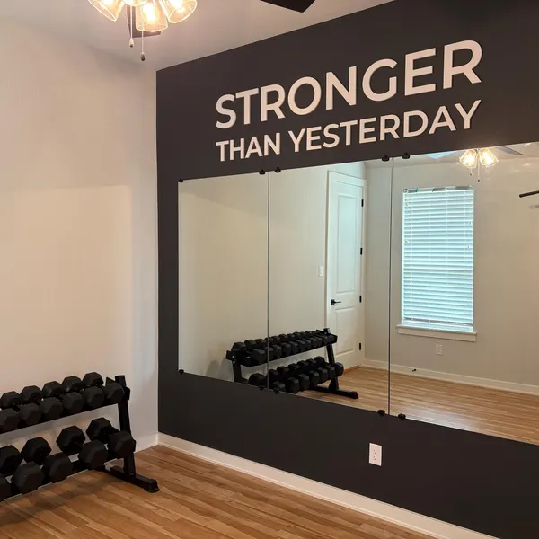 STRONGER THAN YESTERDAY lettering above mirrors and dumbbells in a customer's gym