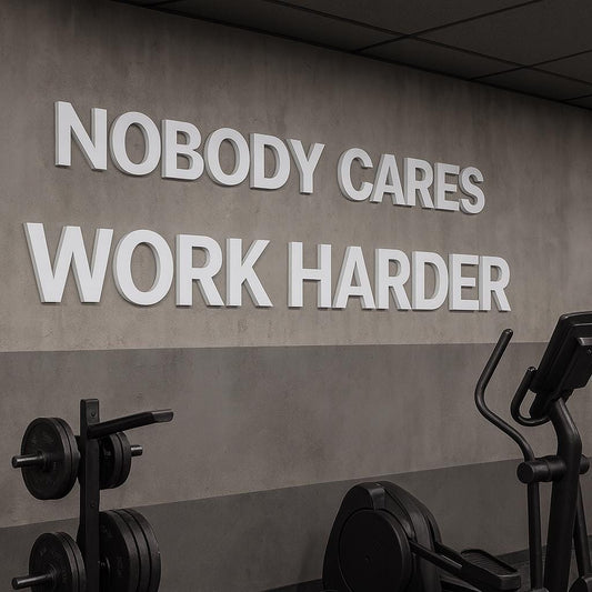 A motivational gym wall art piece with the text "NOBODY CARES WORK HARDER" in white block letters. The image includes exercise equipment such as weights and an elliptical machine, set against a gray wall.